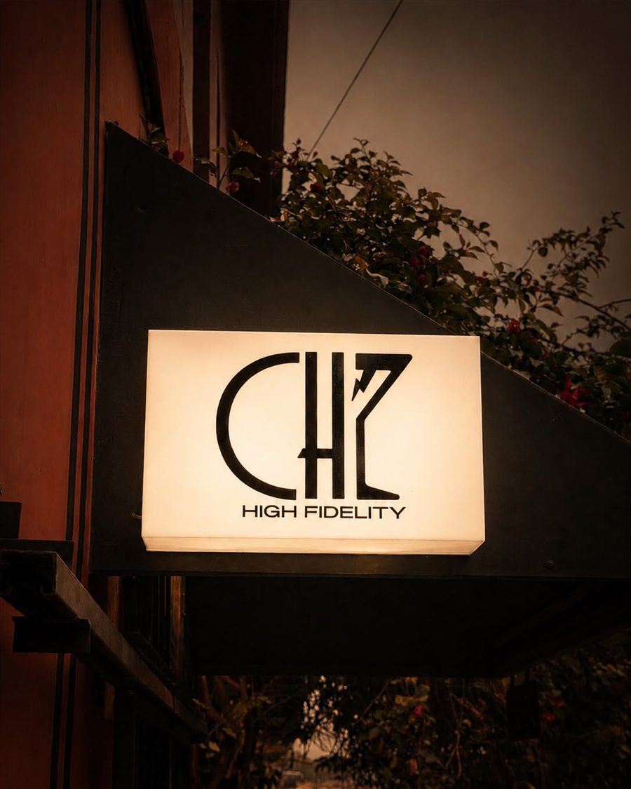 Gabinete luminoso rectangular con el logotipo de CHZ High Fidelity, encendido en luz cálida sobre una fachada de noche.