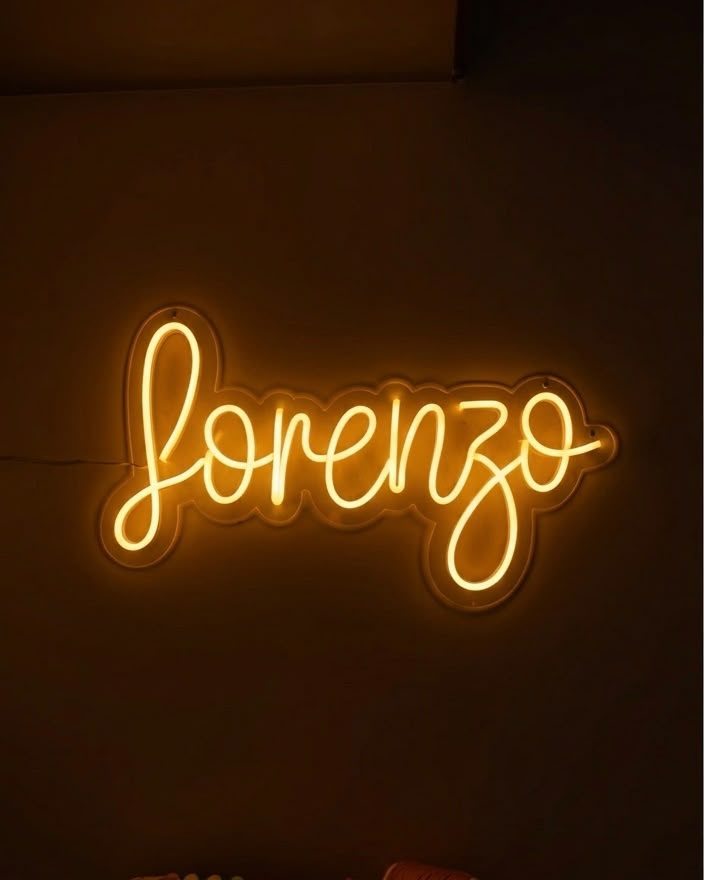 Neón cálido en letra cursiva con el nombre Lorenzo, encendido sobre un muro en penumbra.