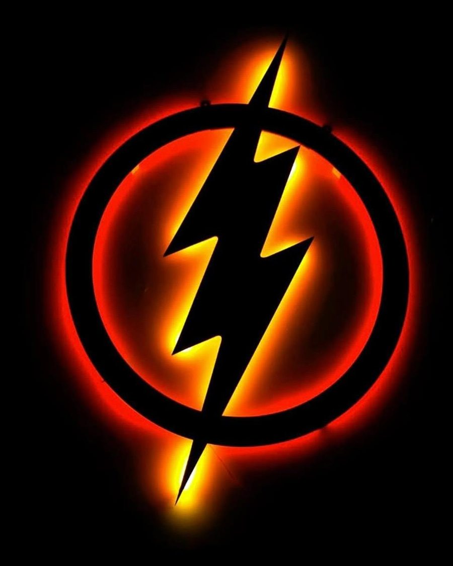 Emblema circular con un rayo, cortado en pieza negra y retroiluminado en rojo y ámbar sobre un muro oscuro.